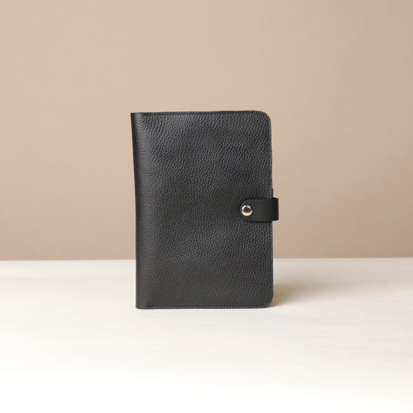 Front view of a black Danilos pebble leather inskspirator with a clip closure on a beige background