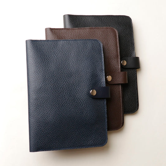 Front view of three Danilos pebble leather inkspirator in blue, black, and brown colors with a clip closure on a beige background