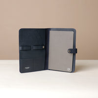 Front view of an open marine blue Danilos pebble leather inkspirator with a clip closure, a black notebook inside, and organized pouches for pens on a beige background