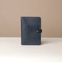 Front view of a marine blue Danilos pebble leather inkspirator with a clip closure on a beige background