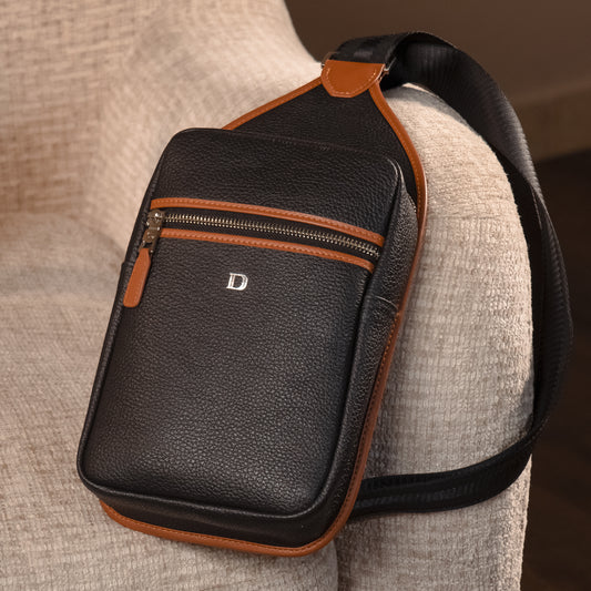 Black leather sling pack Andres with brown accents on a beige surface