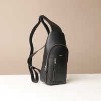 Side view of an open Danilos leather sling pack Andres in a black color with silver zippers on a beige background