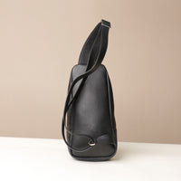 Back view of an open Danilos leather sling pack Andres in a black color with silver zippers on a beige background