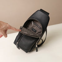 Upper view of an open Danilos leather sling pack Andres on a black color with silver zippers on a beige background
