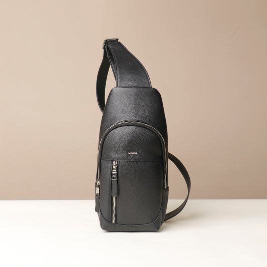 Front view of an open Danilos leather sling pack Andres in a black color with silver zippers on a beige background