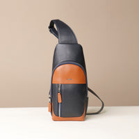 Front view of a Danilos leather sling pack Andres on a marine blue and brown color with silver zippers on a beige background