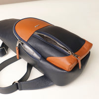 Close-up view of an open Danilos leather sling pack Andres on a marine blue and brown color with silver zippers on a beige background