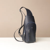 Side view of an open Danilos leather sling pack, Andres in a marine color with silver zippers on a beige background