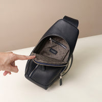 Upper view of an open Danilos leather sling pack, Andres in a marine color with silver zippers on a beige background