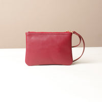 Red leather wristlet pouch bag with a strap on a beige background