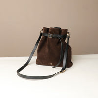 Brown suede leather bucket Danilos bag with long black strap for crossbody on a beige background