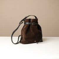 Brown suede leather bucket Danilos bag with black strap on a beige background