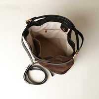 Upper view of a opened brown suede bucket Danilos bag with black strap on a light beige background