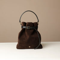 Brown bucket Danilos bag with black handle and strap on a beige background