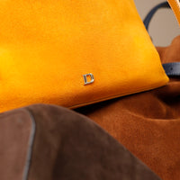 Close up of a Yellow suede leather bucket bag with a Danilos logo on a brown surface