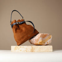 Brown suede leather bucket Danilos bag with black handle on a beige rock against a beige background