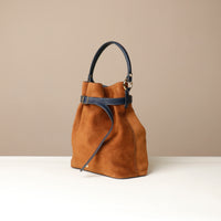 Brown suede suede bucket Danilos bag with black handle on a beige background