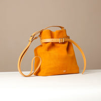 Mustard yellow suede leather bucket Danilos bag with a strap on a light gray background