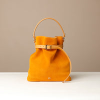 Mustard yellow suede leather bucket Danilos bag with gold accents on a beige background