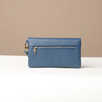 Back view of a blue leather Karelia Clutch Danilos with a visible gold zipper over a white and beige background