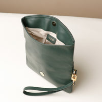 Upper view of an open green leather Karelia Clutch Danilos with a visible hand strap over a white and beige background