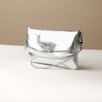 Side view of a silver leather Karelia Clutch Danilos with a visible hand strap over a white and beige background