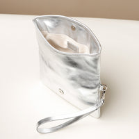 Upper view of an open silver leather Karelia Clutch Danilos with a visible hand strap over a white and beige background