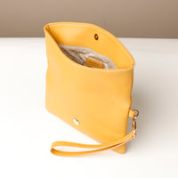 Upper view of an open yellow leather Karelia Clutch Danilos with a visible hand strap over a white and beige background