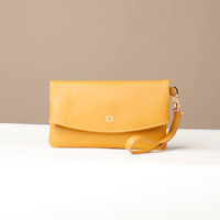 Front view of a yellow leather Karelia Clutch Danilos with a visible hand strap over a white and beige background