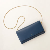 front view of a danilos clucth versaviva in blue leather with a gold chain strap in a beige background