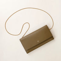 front view of a danilos clucth versaviva in green leather with a gold chain strap in a beige background