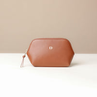 Brown leather pouch with a gold zipper and 'D' logo on a beige background