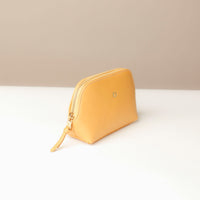 Yellow pouch with a gold zipper on a white surface with a beige background