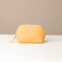 Yellow cosmetic pouch with a brand logo on a white surface and beige background