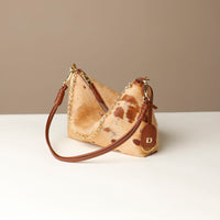 Cowhide Danilos handbag with gold chain and brown leather strap on a white surface with beige background