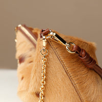 Close-up of a brown fur Danilos bag with a gold chain and leather strap on a neutral background