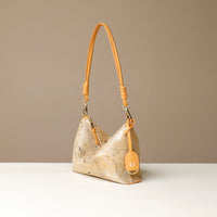 Gold crossbody Danilos bag with a strap on a beige background