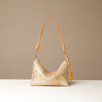 Gold and yellow crossbody Danilos bag with a textured snake surface on a beige background