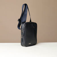side view of a danilos navy blue crossbody dylan bag over a beige background