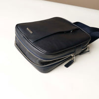 close up view of a open expandable zipper pocket of a danilos navy blue crossbody dylan bag over a beige background