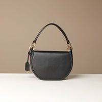 Black Danilos round hair on leather  handbag with gold accents on a beige background