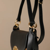 Black Danilos round hair on leather  handbag with gold accents on a beige background