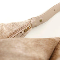 Close-up of a beige hair on Danilos leather handbag with a gold zipper on a white background
