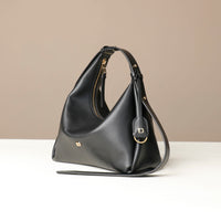 Black leather Danilos handbag with gold accents on a beige background