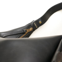 Close-up of a black leather bag with gold zipper and 'Danilos' branding on a white background