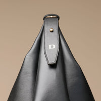 Black leather handbag with a strap featuring the Danilos logo on a beige background