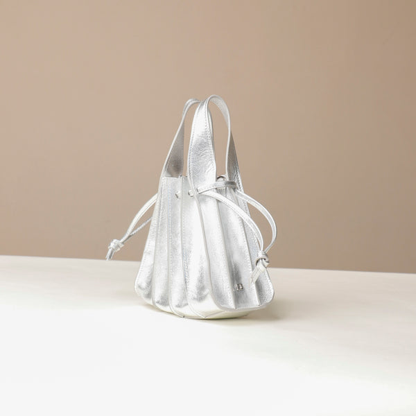 Side view of a Danilos Handbag mini papillon junior in metallic silver color leather over a beige background