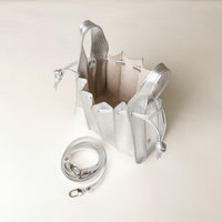 upper view of an open Danilos Handbag mini papillon junior in metallic silver color leather with a visible strap over a beige background