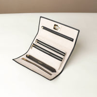 Front view of the Danilos Leather jewelry organizer Mishka in black with gold zippers and organizing pockets, in a beige background