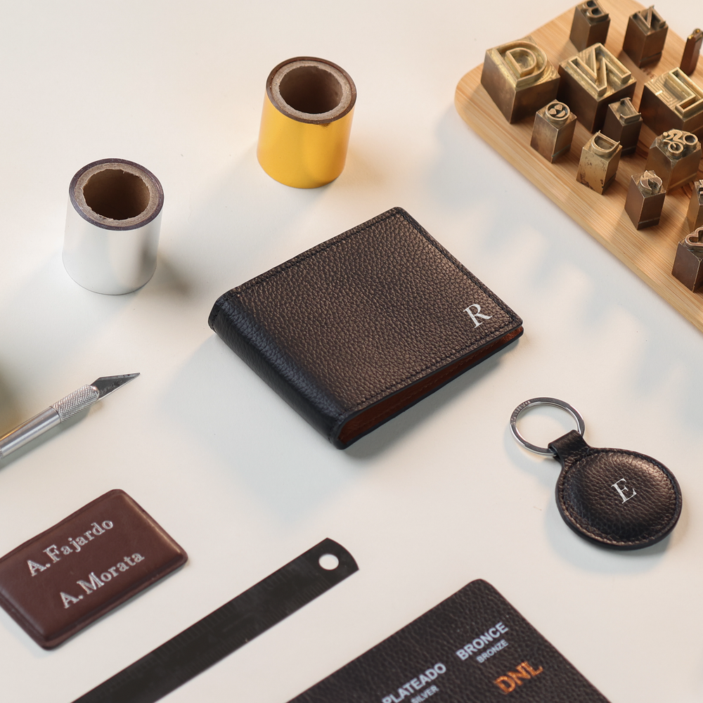 upper view of a Danilos pebble black leather money clip steven with monogram tools around in a white background